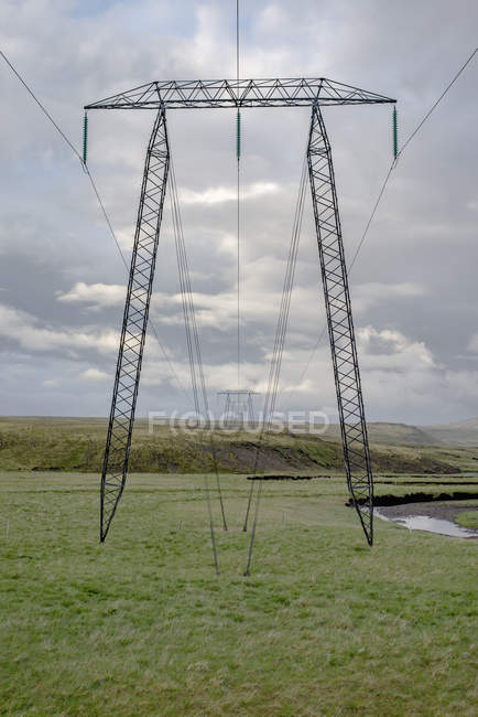 Pilones de electricidad industrial en el campo verde contra el cielo nublado - foto de stock