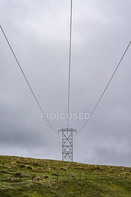 Vista a basso angolo del pilone elettrico sul campo verde contro il cielo nuvoloso — Foto stock