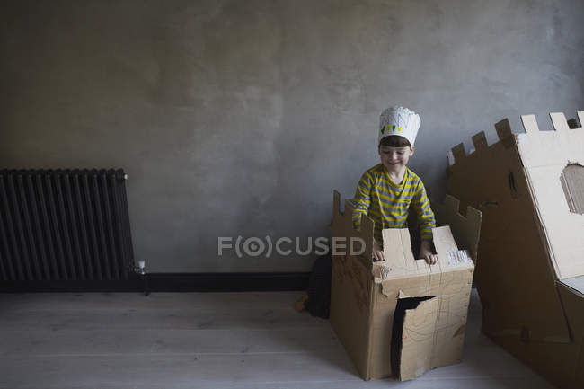 Niño feliz jugando con caja de cartón por pared - foto de stock