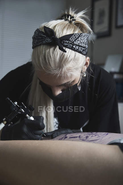 Artist wearing mask tattooing on customer's leg at art studio — Stock Photo
