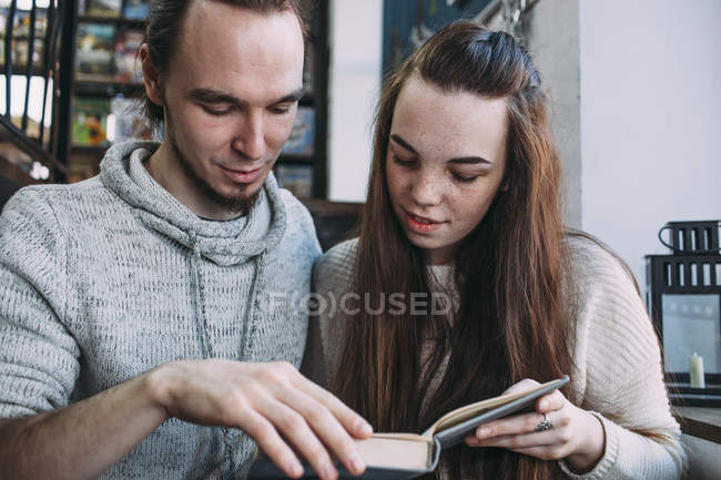 Joven pareja leyendo libro mientras está sentado en la cafetería - foto de stock