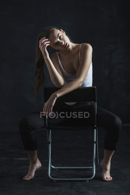Ritratto di giovane ragazza di moda seduta su una sedia sullo sfondo nero — Foto stock