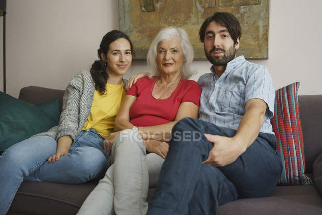 Retrato madre mayor sentada con hija e hijo en el sofá de la sala de estar - foto de stock