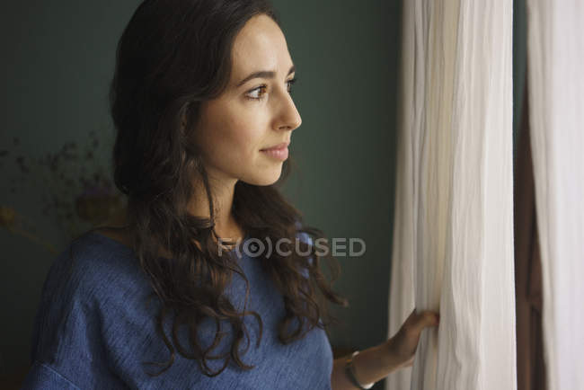 Mujer curiosa de pie en la ventana, esperando - foto de stock
