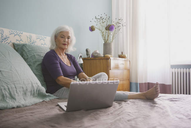 Donna anziana utilizzando il computer portatile sul letto — Foto stock