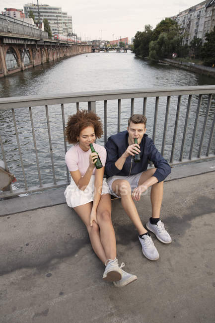 Giovane coppia bere birra sul ponte urbano sul fiume — Foto stock