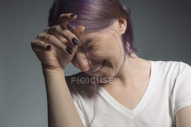 Mujer joven con el pelo teñido mirando hacia otro lado y haciendo una mueca contra el fondo gris - foto de stock