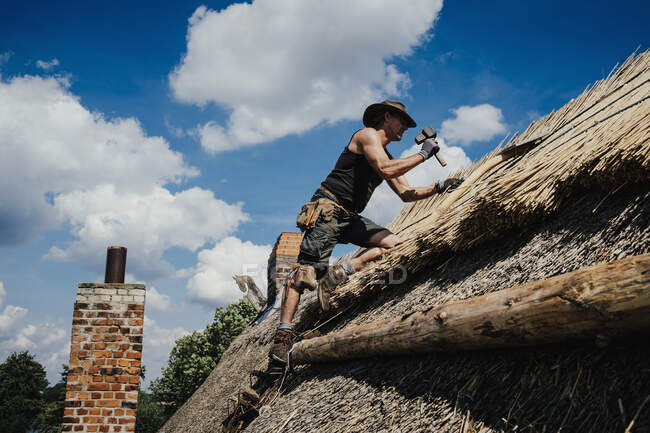 Man repairing thatch roof on sunny house — Stock Photo