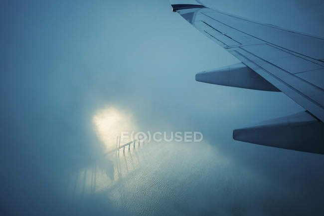 Крыло самолета летит через облака над водой — стоковое фото