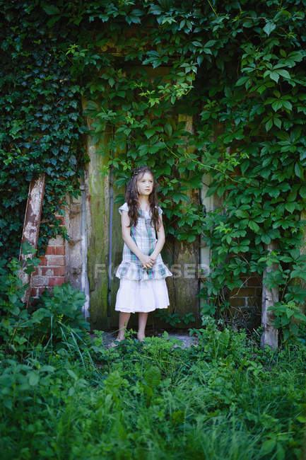 Serena ragazza in abito in piedi alla porta rustica ricoperta di edera verde — Foto stock