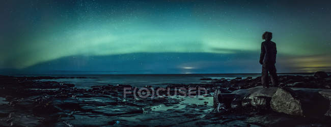 Adolescente viendo Northern Lights desde la roca, Reykjanesbaer, Islandia - foto de stock