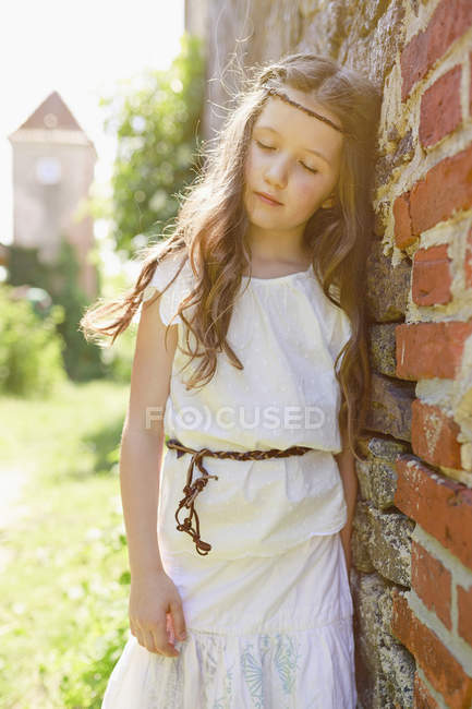 Спокойная девушка в платье, прислонившаяся к кирпичной стене — стоковое фото