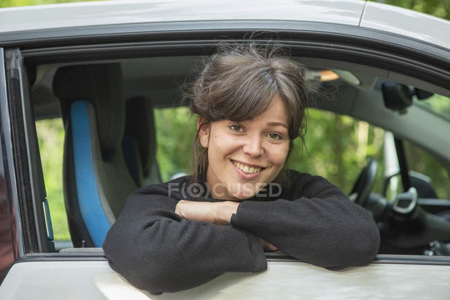 Retrato de sorrir jovem mulher inclinando-se para fora janela do carro — Fotografia de Stock