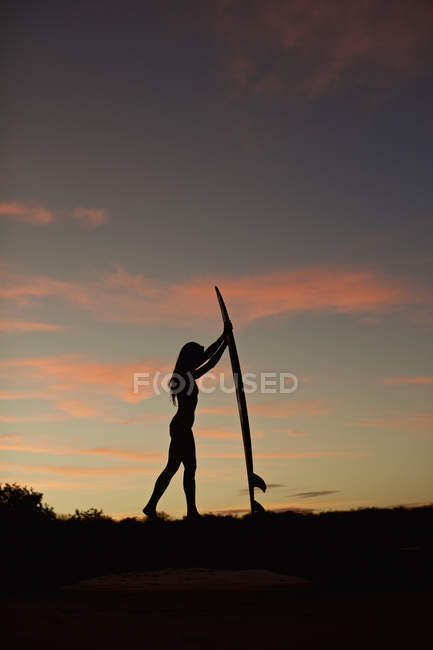Silhouette di surfista donna con tavola da surf sulla spiaggia al tramonto — Foto stock