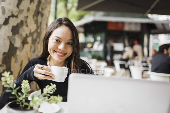 Portrait of confident woman drinking coffee at laptop on sidewalk cafe — Stock Photo