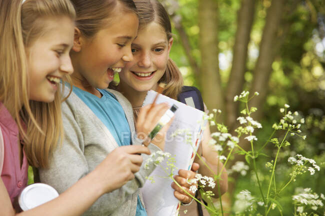 Chicas sonrientes con lupa examinando flores en viaje de campo - foto de stock