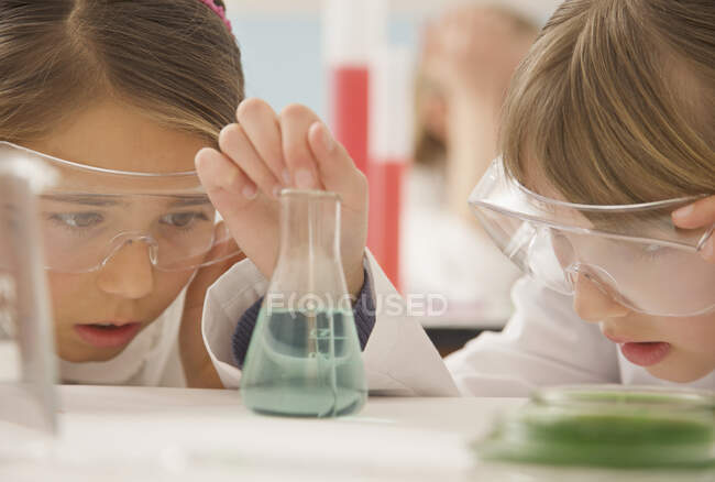 Curieux lycéennes étudiantes examinant liquide en bécher de science — Photo de stock