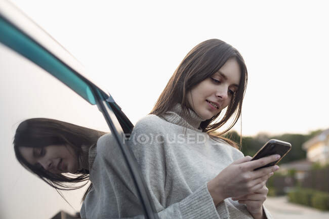 Jeune femme utilisant un téléphone intelligent extérieur voiture — Photo de stock