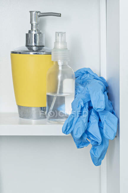 Guantes protectores en el estante del baño con jabón y desinfectante - foto de stock
