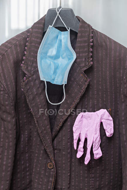 Máscara protectora y guantes colgando de la chaqueta del traje - foto de stock