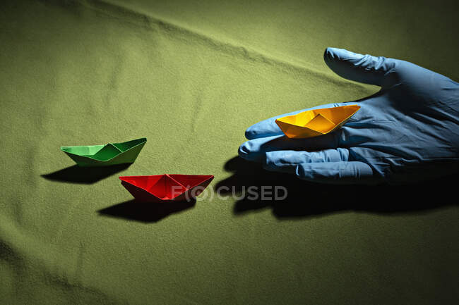 Mano en guante protector sosteniendo barco de origami - foto de stock