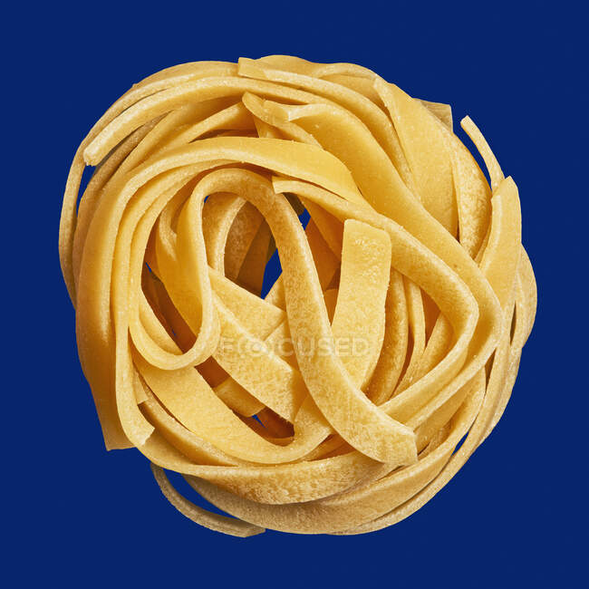 Close up ninho de macarrão espaguete não cozido no fundo azul — Fotografia de Stock