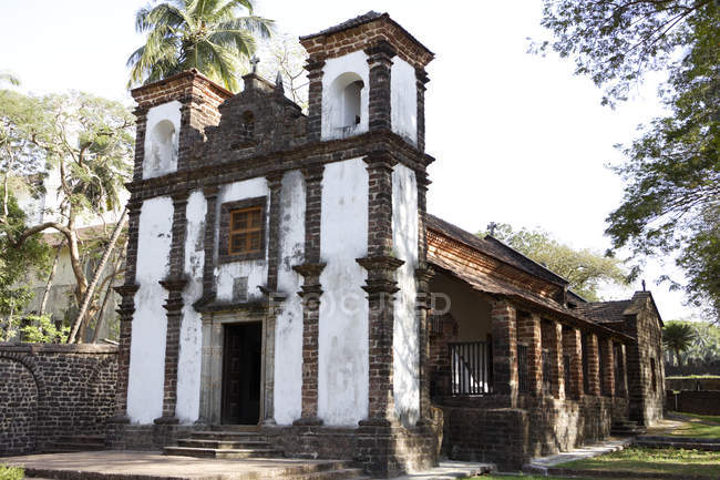 Seitenansicht der Kapelle der hl. Katherine, die tagsüber von Palmen über grünem Gras umgeben ist, Goa, Indien — Stockfoto