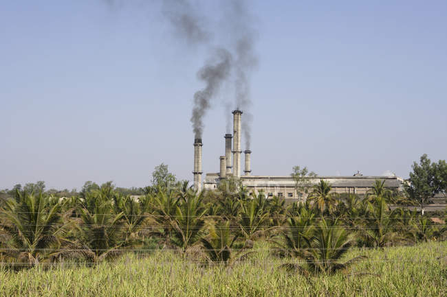 Fabbrica di zucchero con fumo ed erba verde sul davanti, Karnataka, India — Foto stock
