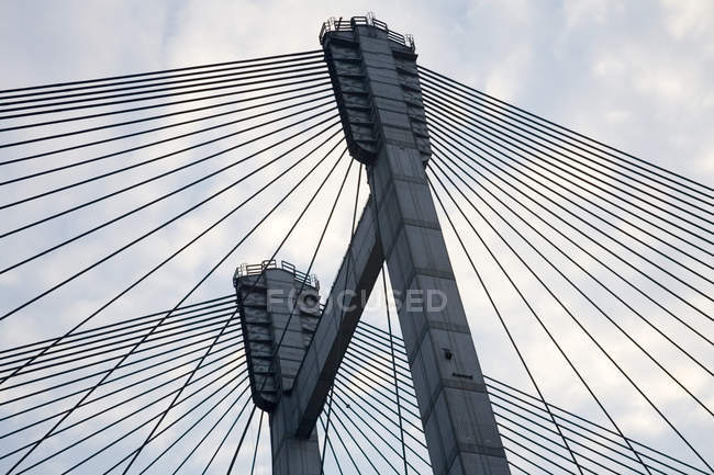 Vue en angle bas de la construction du pont avec des fils contre le ciel nuageux le soir — Photo de stock