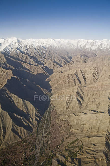Вид снега с воздуха покрыл Гималайские горы домами и полями вдоль реки в долине на переднем плане, как видно на полете из Дели в Лех-Ладакх. Индия — стоковое фото