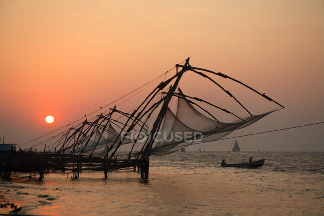 Vista do pôr do sol na praia de areia com redes em construção contra a água, Ernakulam District, Kerala, Índia
. — Fotografia de Stock