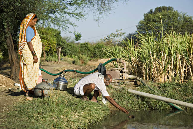 Granjero con su esposa tomando agua en el recipiente del estanque de agua. Salunkwadi, Ambajogai, Beed, Maharashtra, India - foto de stock