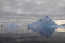 Iceberg y cielo nublado reflejados en el agua - foto de stock