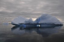 Iceberg y cielo nublado reflejados en el agua - foto de stock