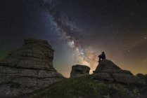 Hombre sentado en la cima de la montaña Demerdzhi bajo la Vía Láctea por la noche en Alushta, Crimea - foto de stock
