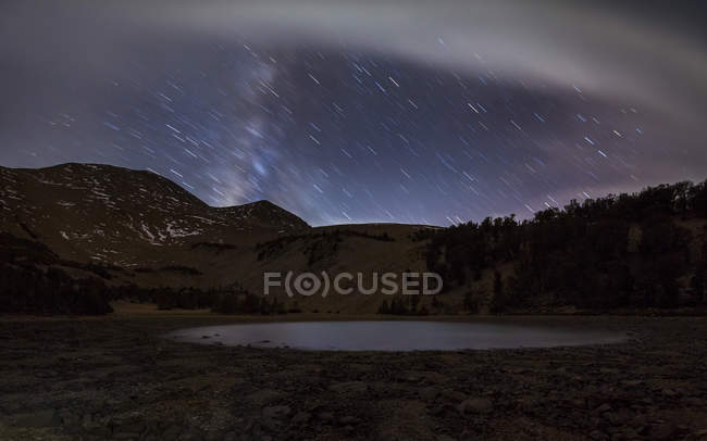 Star trails above small lake — Stock Photo