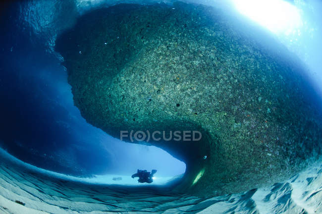 Immergitore che nuota intorno ad una grande formazione rocciosa in una caverna aperta sulla costa orientale della Sardegna — Foto stock