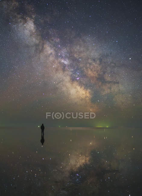 Hombre de pie bajo el centro de la Vía Láctea y estrellas reflejadas en el lago Elton, Rusia - foto de stock