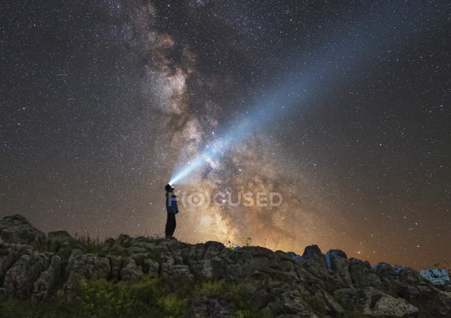 Man standing on rocks of Lago-Naki plateau and shining flashlight on Milky Way, Russia — Stock Photo