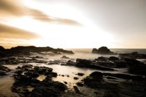 Longue exposition, mer, lumière du soir avec nuages mousseux et rochers rugueux — Photo de stock