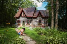 Boy squatting on a path to a log cabin cottage on a summer day. — Stock Photo
