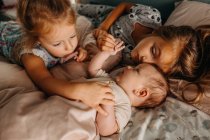 Duas meninas tocando bebê irmão e abraçando na cama juntos — Fotografia de Stock