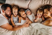 Große Familie liegt mit vielen Kindern im Bett und hält Händchen — Stockfoto