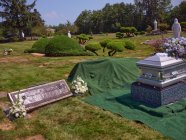 Um caixão com flores fica ao lado de um túmulo pronto para o enterro. — Fotografia de Stock