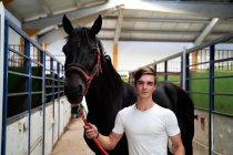 Молодий чоловік позує зі своїм конем перед класом їзди — стокове фото