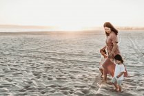 Mãe andando com 2 anos de idade menina na praia durante o pôr do sol — Fotografia de Stock