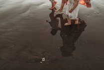 Reflexão na água do oceano da mãe andando duas filhas na praia — Fotografia de Stock