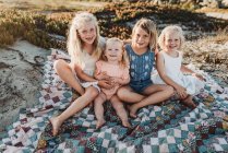 Quatro irmãs sentadas em cobertor na praia sorrindo ao pôr do sol — Fotografia de Stock