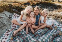 Чотири сестри сидять на ковдрі на пляжі, посміхаючись на заході сонця — стокове фото