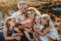 Lifestyle close up of family with young sisters sitting on beach — Stock Photo